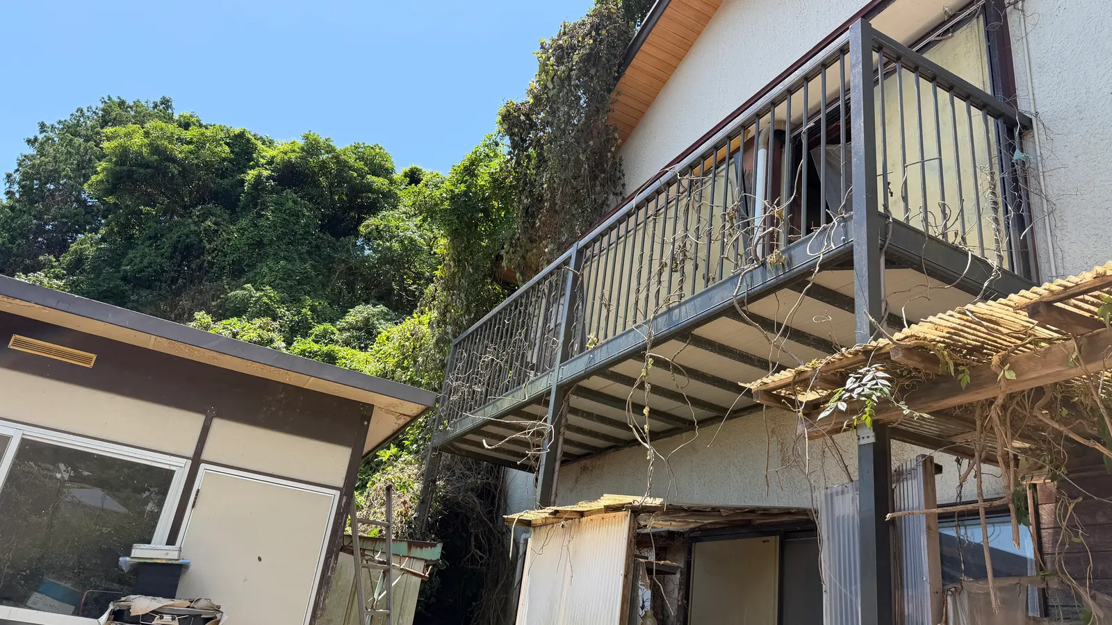 木立の斜面を背にした古い2階建ての家