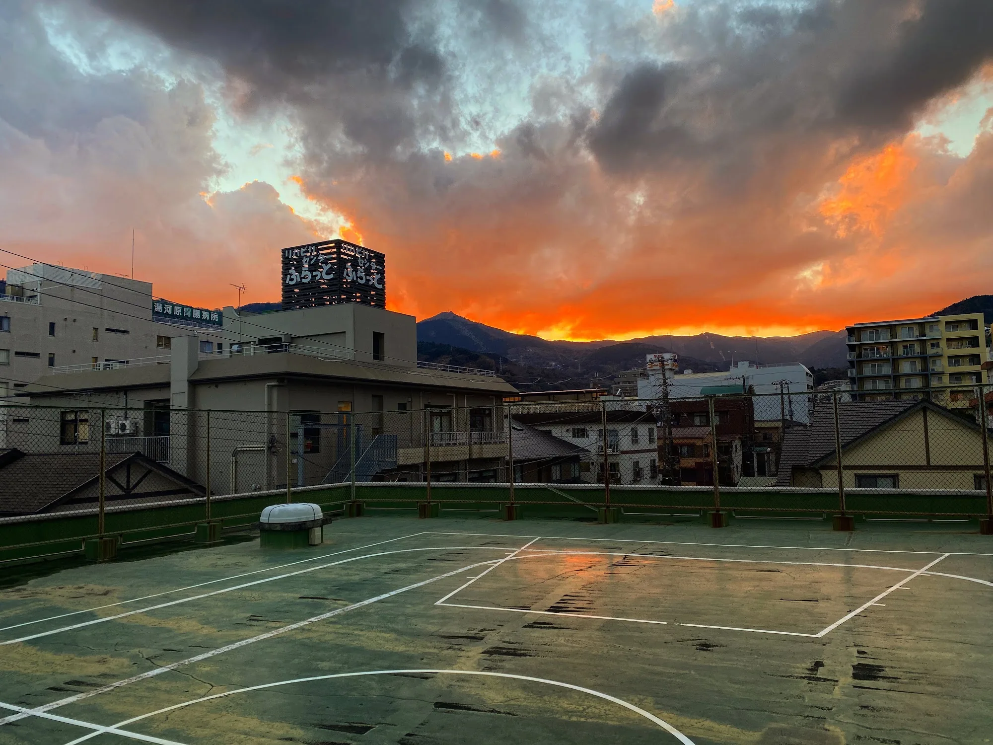 夕焼けの屋上。町の背後の山に、オレンジ色の雲がかかる