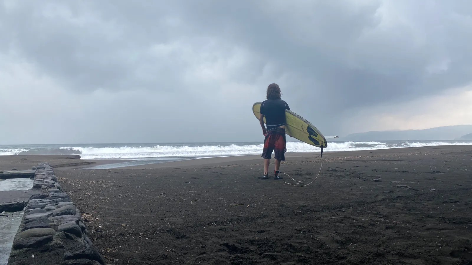 吉浜の黒い砂浜で波を見るサーファー