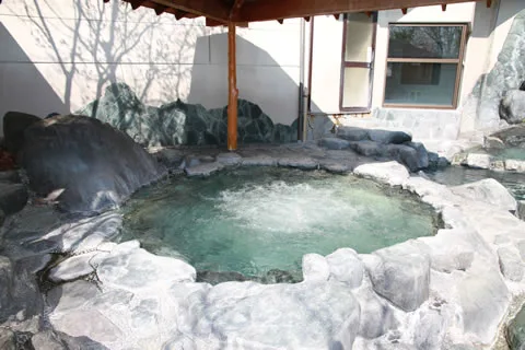 木の屋根の下の丸い岩風呂